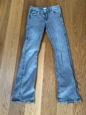 Grå bootcut jeans med fem fickor - Säljer ett par grå jeans med bootcut-modell och klassisk femficksdesign. Jeansen har bälteshällor, knappgylf och är tillverkade i ett mjukt denimtyg. Perfekta för dig som gillar en avslappnad men ändå snygg stil.