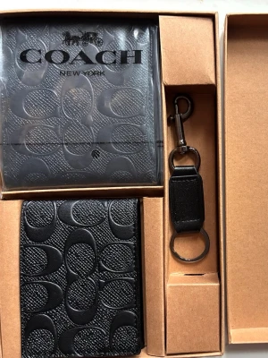 Svart plånbok från Coach - Snygg svart plånbok från Coach i präglat läder med det klassiska C-mönstret. Kommer i presentförpackning tillsammans med en matchande nyckelring. Perfekt accessoar för dig som gillar stilrena detaljer och exklusiv känsla.