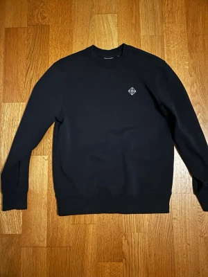 Svart Lindeberg sweatshirt  - En stilren svart Grish sweatshirt med rund hals och en liten diskret logga på bröstet. Tröjan har långa ärmar och ribbade muddar vid ärmslut och nederkant. Perfekt för en clean och enkel look.