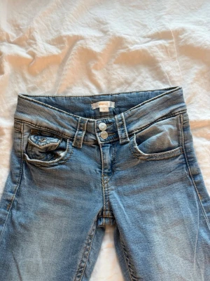 Blå jeans med dubbla knappar - Säljer ett par ljusblå jeans från Gina Tricot Young med dubbla knappar i midjan. I storlek 152 färg blå