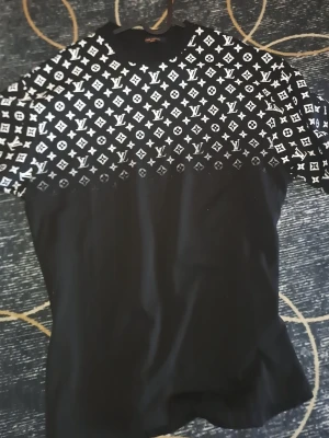 Svart t-shirt med vit logomönster - Säljer en svart t-shirt med korta ärmar och ett stort vitt logomönster över bröst och axlar. T-shirten har en klassisk passform och är tillverkad i mjukt bomullstyg. Perfekt för dig som gillar streetwear och vill sticka ut.