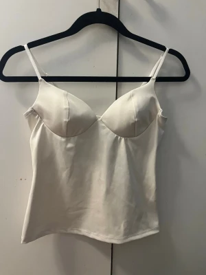 Vit shaping body med tunna band - Snygg vit shaping body med tunna, justerbara axelband och vadderade kupor. Tillverkad i ett slätt, stretchigt material som ger en smickrande siluett. Perfekt under tighta plagg för en clean look.