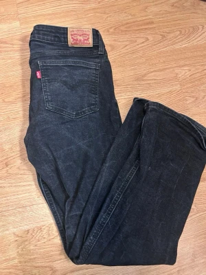 Levi's svarta bootcut jeans 28 - Snygga svarta jeans från Levi's i modellen Superlow Boot. Jeansen har klassisk femficksdesign, låg midja och bootcut-ben. Tillverkade i slitstark denim med en diskret tvättad look och Levi's ikoniska röda etikett på bakfickan.