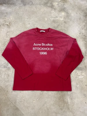 Röd långärmad t-shirt Acne Studios - Snygg röd långärmad t-shirt från Acne Studios med vit text 'Acne Studios STOCKHOLM 1996' på bröstet. Klassisk passform och rund halsringning, perfekt för en stilren och avslappnad look. Storlek M