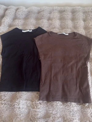 Två baslinnen i svart och brunt - Säljer två stilrena baslinnen i svart och brunt. Båda har rund halsringning och är ärmlösa med rak passform. Perfekta att matcha till olika outfits och tillverkade i mjuk bomull för skön känsla hela dagen. Knappt använda!