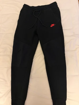 Svarta nike tech byxor med röd logga - Svarta Nike byxor i väldigt bra skicka. Använda maximalt 10 gånger. Har tyvär inte tröjan. Kan gå ner i pris vid snabbaffär.