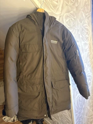 Svart parkas från Peak Performance - Säljer en svart parkas från Peak Performance med dragkedja och tryckknappar, flera praktiska fickor och justerbara muddar. Jackan har en hög krage och är perfekt för kalla dagar. Klassisk och stilren design som passar till det mesta. Stolek S