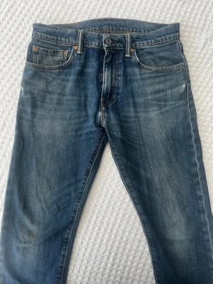 Levi's 512 blå slim jeans - Snygga blå Levi's 512 jeans i slim fit med klassisk femficksdesign och lätt slitna detaljer. Jeansen har mellanblå tvätt och är tillverkade i bomull med en liten mängd stretch för extra komfort. W30 L34