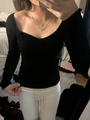 Svart ribbad långärmad topp - Säljer en svart ribbad topp med lång ärm och snygg v-ringad urringning. Toppen har en tight passform och är perfekt att styla med både jeans och kjol. Materialet känns mjukt och stretchigt, vilket gör den bekväm att bära.