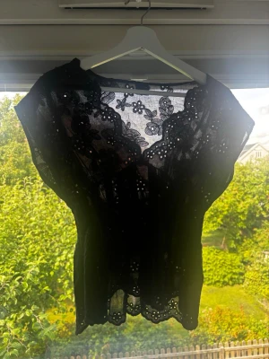 Svart spetsblus med blommönster från gina - Säljer en svart blus i spets med vackert blommönster och broderade detaljer. Blusen är genomskinlig och har korta ärmar samt v-ringad hals. Perfekt för dig som vill ha en feminin och trendig topp med fina detaljer. bara änvänd bara en gång innan, skicka gärna prisförslag😽