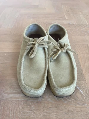 Clarks mocka loafers med snörning - Säljer ett par stilrena beige loafers i mocka med klassisk snörning framtill och mjuk sula. Skorna har en fyrkantig tå och låg profil, perfekta för en avslappnad men ändå trendig look.