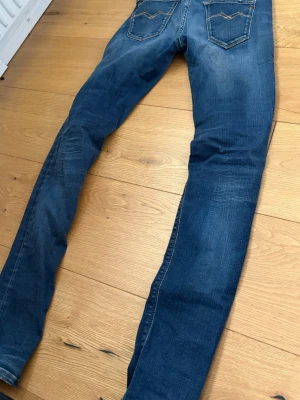 Blå slim fit jeans med slitningar - Säljer ett par blå slim fit jeans med snygga slitningar och tvättade detaljer på benen. Jeansen har klassisk femficksdesign och kontrastsömmar. Perfekta för dig som gillar en avslappnad men trendig stil.