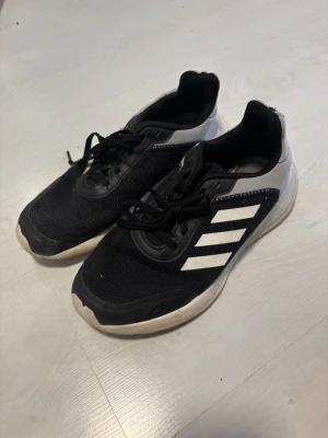 Svarta Adidas sneakers med vita ränder - Snygga svarta Adidas sneakers med klassiska vita ränder på sidan och vit sula. Ovandelen är i mesh-tyg för bra ventilation och skon har svarta skosnören. Perfekta för en sportig och avslappnad stil.