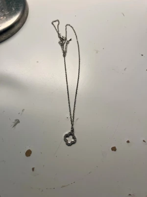 Silverfärgat halsband med blomma - Snyggt halsband i silverfärg med en tunn kedja och ett hängsmycke format som en blomma. Hängsmycket har små pärldetaljer runt hela formen som ger ett elegant intryck. Perfekt för dig som gillar stilrena accessoarer med en twist.