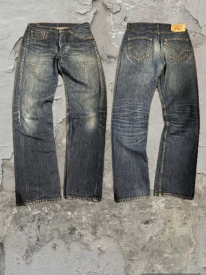 Levis jeans 501 - Säljer ett par blå jeans med raka ben och snygga slitningar på framsidan och baksidan. Jeansen har klassisk femficksmodell, kontrastsömmar och en vintage tvättad look. Perfekta för en avslappnad och trendig stil.