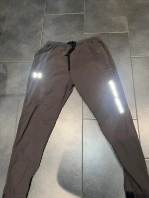 Svarta träningsbyxor Under Armour - Säljer ett par svarta träningsbyxor från Under Armour med reflexdetaljer och dragsko i midjan. Byxorna har smal passform och är tillverkade i ett lätt, snabbtorkande material som passar perfekt till löpning eller gym. Passar även L 