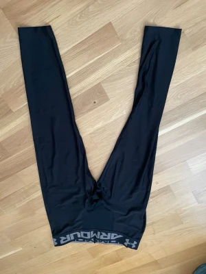 Svarta leggings från Under Armour - Snygga svarta leggings från Under Armour med logga på benet och bred resår i midjan med text. Tillverkade i stretchigt funktionsmaterial som passar perfekt till träning eller chill. Tight passform och klassisk look.
