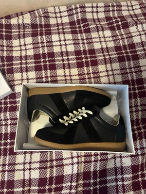 Svarta sneakers med vit sula - Snygga svarta sneakers med vita skosnören och ljusbrun gummisula. Skorna har en klassisk låg profil och är tillverkade i en mix av mocka och läder. Perfekta för dig som gillar stilrena och tidlösa sneakers.