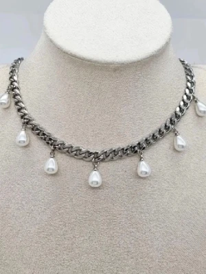Kedjehalsband med droppformade pärlor - Snyggt halsband i silverfärgad metall med droppformade vita pärlor som hänger längs hela kedjan. Kedjan har en chunky design som ger ett trendigt och modernt intryck. Perfekt accessoar för att lyfta din outfit.