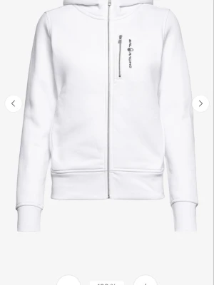 Vit hoodie med dragkedja Sail Racing - Snygg vit hoodie från Sail Racing med hel dragkedja framtill och en bröstficka med vertikal dragkedja. Hoodien har ribbade muddar vid ärmslut och nederkant samt en stilren logga på bröstet. Perfekt för en clean och sportig look.