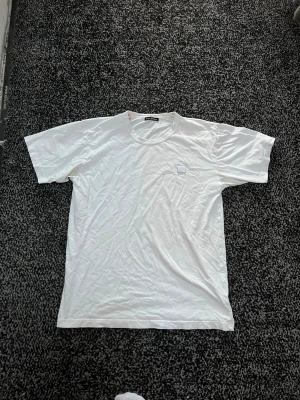 Vit t-shirt från Acne Studios - Klassisk vit t-shirt från Acne Studios med rund hals och diskret logopatch på bröstet. Tillverkad i mjuk bomull och har en normal passform. Perfekt basplagg för alla tillfällen.