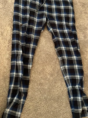 Rutiga pyjamasbyxor i blått och svart - Mysiga pyjamasbyxor med rutigt mönster i blått, svart och vitt. Byxorna har en avslappnad passform och resår i midjan för extra komfort. Perfekta för chillkvällar hemma eller när du vill vara extra bekväm.