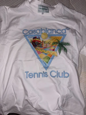 Vit Casablanca Tennis Club t-shirt - Snygg vit t-shirt från Casablanca med färgglatt tryck och texten 'Tennis Club' framtill. T-shirten har rund hals och korta ärmar, perfekt för en avslappnad och sportig stil.