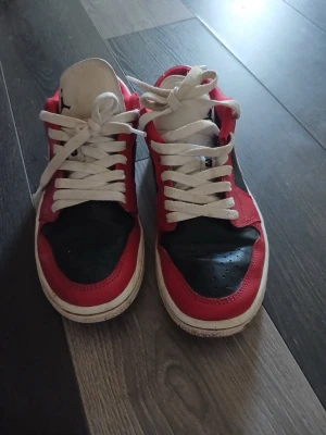 Nike Dunk Low röd/svart/vit - Säljer ett par jordan 1 low sneakers i rött, svart och vitt. Skorna har klassisk låg siluett, vit sula och vita skosnören. Ovandelen är i läder med svart tåparti och röda paneler, samt vit Nike Swoosh på sidan. Perfekta för dig som gillar streetwear och snygg design.  Låda dinns inte