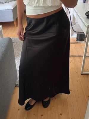 Svart långkjol i satin - Svart långkjol i satin från Vero Moda. Kjolen har en slät yta och lätt glans, storlek M, aldrig använd. 
