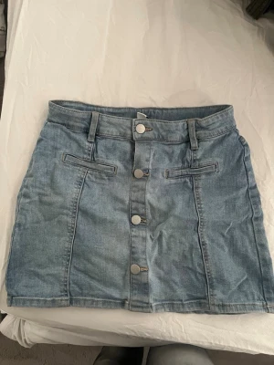 Ljusblå jeanskjol med knappar - Jeanskjol från Lindex passar mig som är 162 lång och brukar ha storlek S i kläder och skulle säga att de passar storlek S och man kan även justera hur man vill ha den i midjan.
