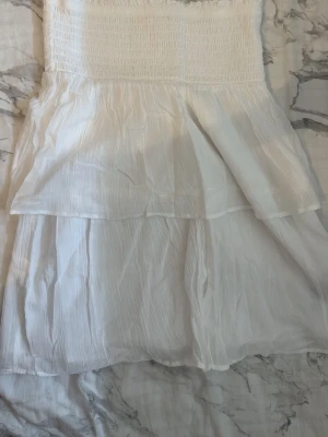 Vit sommarklänning från Gina Tricot - Söt vit klänning från Gina Tricot med smock upptill och dubbla lager i kjolen. Klänningen är axelbandslös och har en luftig, lätt struktur som passar perfekt till varma dagar. Materialet känns mjukt och bekvämt mot huden. Priset går att diskutera! 