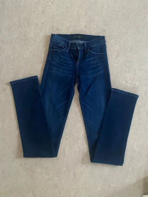 Mörkblå jeans Goldsign - Snygga mörkblå jeans från Goldsign med klassisk femficksmodell och hög midja. Jeansen har en stilren look med smala ben och är tillverkade i stretchigt denimtyg för extra komfort. Perfekta till alla dina favoritoutfits! Storlek W24