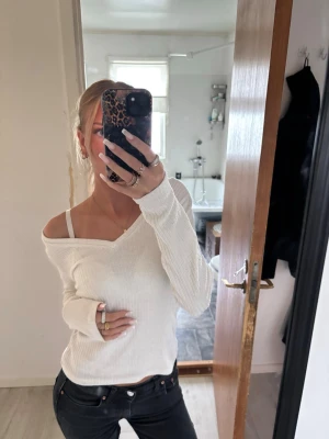 Vit ribbad offshoulder topp - Trendig vit ribbad topp med offshoulder-design och lång ärm. Toppen har en avslappnad passform och är perfekt att styla med jeans eller kjol. Materialet känns mjukt och följsamt mot huden.