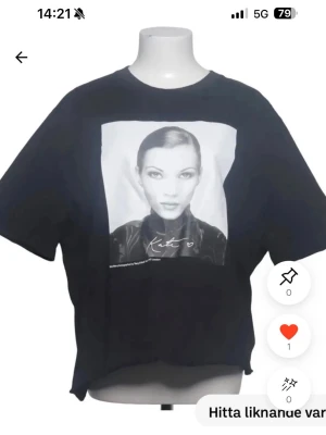 Kate moss t-shirt  - Cool svart t-shirt med stort fototryck av ett ansikte på bröstet och texten 'Kate' under bilden. T-shirten har en avslappnad passform och klassisk rund hals. Perfekt för dig som gillar statement-plagg och grafiska tryck.