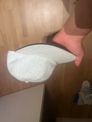 Vit keps med diskret mönster - Snygg vit keps med diskret ton-i-ton mönster och böjd skärm. Justerbar baktill för perfekt passform. Kepsen har en stilren look och passar till många olika outfits. Materialet känns lätt och bekvämt.