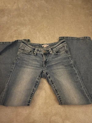 Ljusblå bootcut jeans med strass - Säljer ett par ljusblå bootcut jeans med snygga strassdetaljer på bakfickorna. Jeansen har klassisk femficksmodell, normal midja och är i mjukt denimtyg. Perfekta för dig som vill ha en trendig och bekväm look. Har används max 2 ggr då jeansen inte passar mig så bra. Jeansen är lite ljusare i färgen än på bilderna eftersom dom är tagna i mörkt ljus! Skriv om ni har några frågor. 