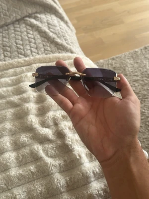 Svarta solglasögon från Givenchy - Snygga solglasögon från Givenchy med svarta bågar och guldiga detaljer på sidorna. Glasen är mörka och rektangulära utan synlig ram runt, vilket ger en clean och modern look. Perfekta för dig som vill sticka ut med en exklusiv accessoar.