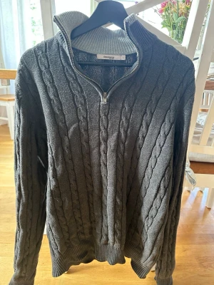 Grå kabelstickad tröja Dressmann - Mörkgrå kabelstickad tröja från Dressmann med halv dragkedja och hög krage. Storlek L. Hör av er vid eventuella frågor.