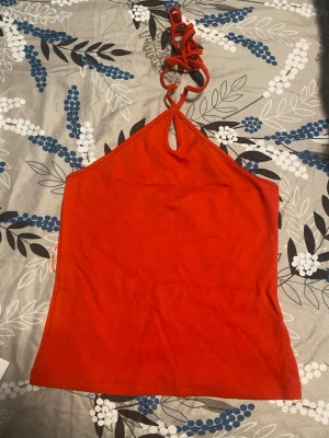 Orange halterneck linnetopp - Snygg orange linnetopp med halterneck och knyt i nacken. Toppen har en liten öppning framtill vid halsen och är ärmlös. Perfekt för varma dagar och enkel att styla med jeans eller kjol.