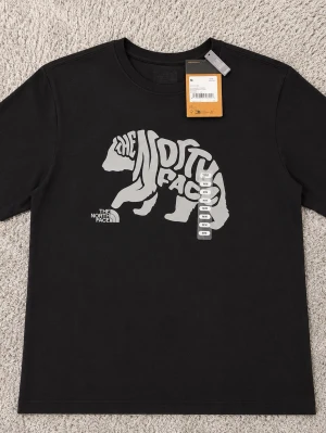 Svart t-shirt The North Face  - Snygg svart t-shirt från The North Face med stor björnprint och logga i vitt på bröstet. Klassisk passform och rund halsringning. Tillverkad i mjuk bomull som känns skön mot huden. Perfekt för dig som gillar streetwear och outdoor-vibe.
