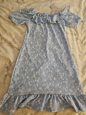 Blommig blå klänning Gina Tricot - Söt blå klänning från Gina Tricot med vitt blommönster, volang vid axlar och nederkant samt korta puffärmar. Perfekt för sommarens alla tillfällen och har en avslappnad passform.