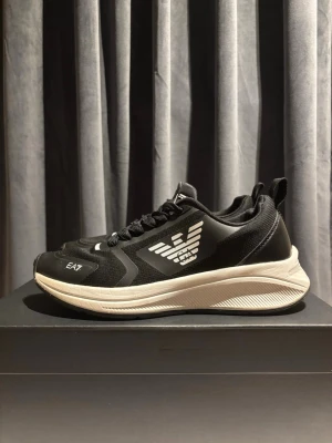 EA7 Skor - Säljer ett par svart/vita EA7 sneakers i fint skick. Har haft dem ett tag men de är sparsamt använda. Lite smuts finns men det fixas innan köp. Sulan är i bra skick och skorna är fortfarande väldigt fräscha. Originalkartong medföljer.