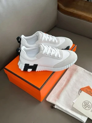 Vita sneakers med svart detalj - Stilrena vita sneakers med tjock sula och svart H-detalj på sidan. Ovandelen är i en mix av mocka och textil, med vita skosnören och dragflik bak. Snygg, modern design som passar till det mesta.