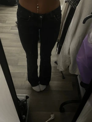 Svarta bootcut jeans - Snygga svarta bootcut jeans med låg midja och klassiska fem fickor. Jeansen har en figurnära passform upptill och lätt utsvängda ben. Perfekta för dig som gillar en retroinspirerad look och vill ha ett par jeans som sitter tajt men ändå är bekväma.