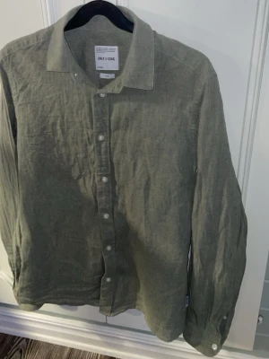 Grön linneskjorta från Only & Sons - Snygg grön skjorta i linne från Only & Sons. Skjortan har klassisk krage, långa ärmar och vita knappar framtill. Perfekt för dig som gillar en avslappnad men stilren look.