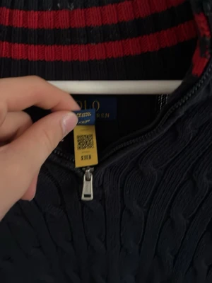 Mörkblå kabelstickad tröja Polo Ralph Lauren xs/s - Mörkblå kabelstickad tröja från Polo Ralph Lauren med halv dragkedja och röd broderad logga på bröstet. Insidan av kragen har röda och svarta ränder. Tröjan har långa ärmar och ribbade muddar. Ny pris 1899kr nästan helt ny!!