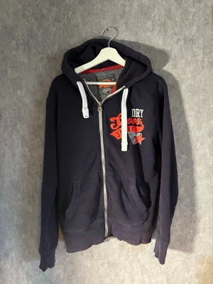 Superdry fullzip hoodie  - Unik superdry fullzip hoodie med lite faded färg samt sprickor i trycket vilket ger den ett vintage utseende. Storlek S men ganska lång i armarna så passar även M. Färgen är mörkblå-lila