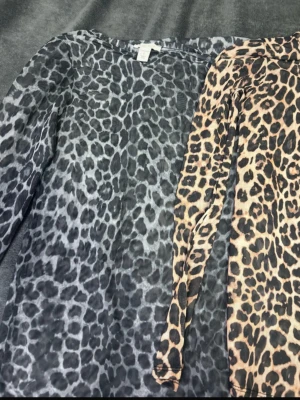 Två mesh-toppar med leopardmönster. Storlekar S/Xs - Säljer två transparenta mesh-toppar med leopardmönster. Ena toppen är i beige och svart, den andra i grå och svart. Båda har lång ärm och tight passform, perfekta för att lyfta vilken outfit som helst.
