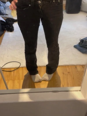 Svarta raka jeans med silverknappar - Säljer ett par svarta jeans med rak passform och klassiska fem fickor. Jeansen har silverfärgade knappar och nitar samt normal midja. Materialet är denim och de har en enkel, stilren look som passar till det mesta.