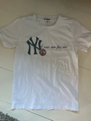 Vit t-shirt med tryck från 2K WRLD - Vit t-shirt från 2K WRLD med stort tryck framtill som inkluderar texten 'new era for me' och en grafisk logga. Klassisk rund hals och korta ärmar. Tillverkad i 100% bomull för en skön och avslappnad känsla. Storlek S men är som en XS